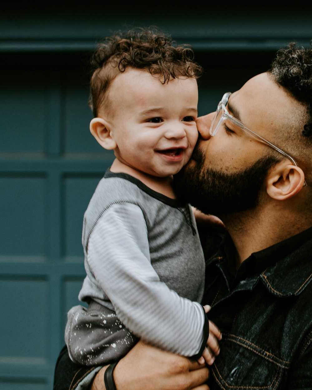 A father holding his laughing son and kissing him on the cheek.